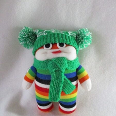 Cool character made rainbow/white striped socks. Wearing machine knitted hat with two pom poms, and matching scarf.